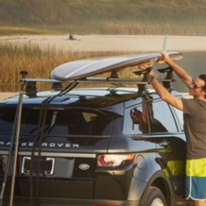 Surfer putting surfboard on vehicle rack