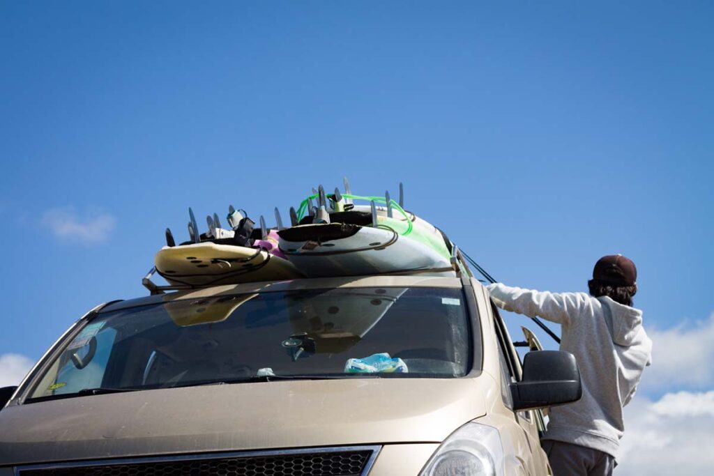 Person tightening surfboards on roof rack.