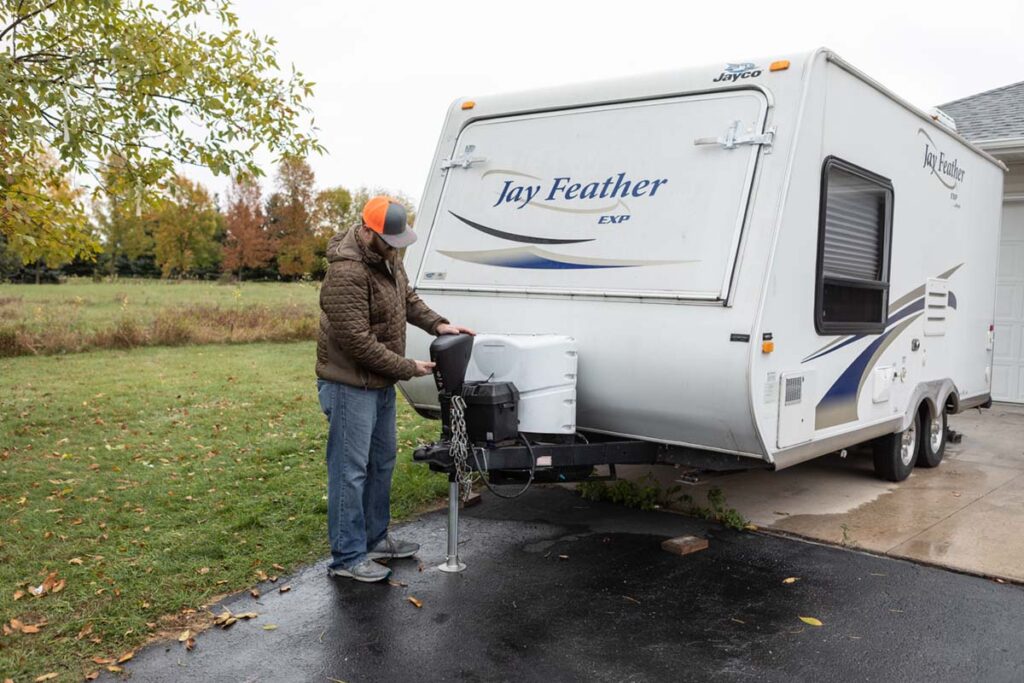 person installing towing accessory on camper